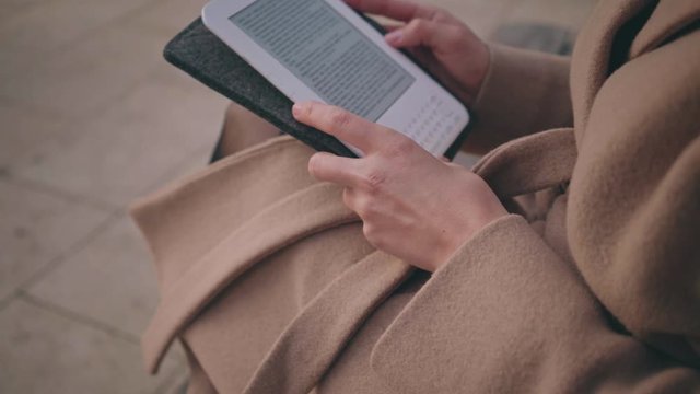 Close up shot of a young female reading through a contemporary futuristic book reader on a chilly autumn day goes through the pages with soft clicks.