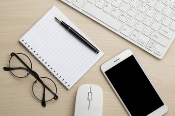 Modern working business desk with keyboard, notepad, smart phone, pen, mouse & glasses. Top view with copy space