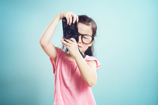 Portrait of cute asian little girl taking picture with retro camera in the studio on vintage mint green background.