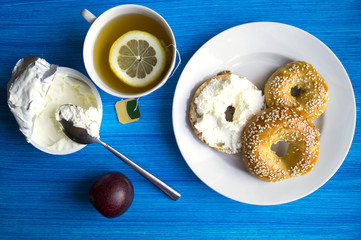 Breakfast at blue table with copy space boundaries. Cream cheese, plum, tea, bagels. The view from the top.