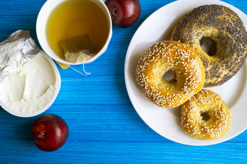 Breakfast at blue table with copy space boundaries. Cream cheese, plum, tea, bagels. The view from the top.