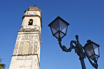 Fototapeta na wymiar Campanile chiesa sullo sfondo di un cielo blu e con primo piano delle lanterne