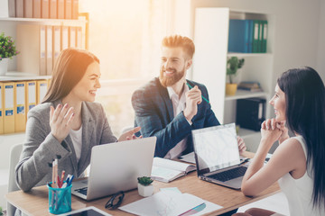 A group of cheerful successful young people discussing business ideas for their company in sunny workspace in formal wear