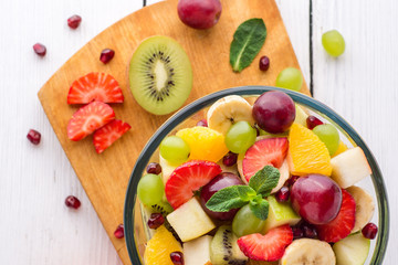 Healthy fresh fruit salad in glass bowl on white wooden background.