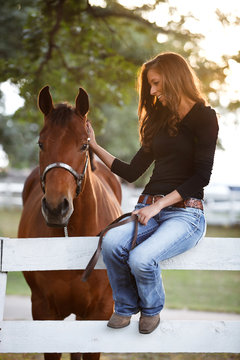 Woman sitting on a fence of a paddock and stroking horse