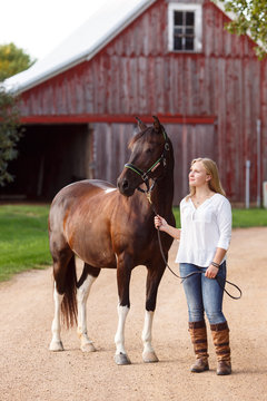 Young woman standing with horse in front of a barn