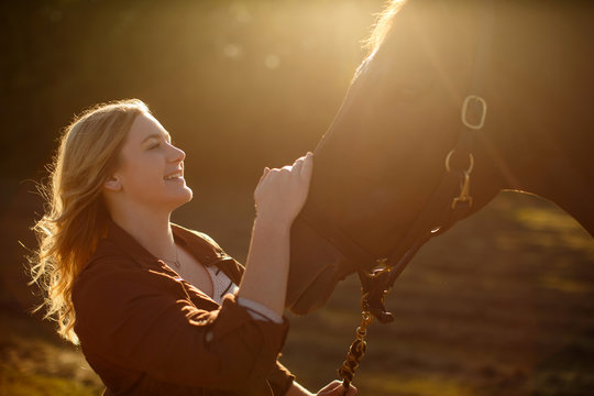 Young woman standing stroking horse, smiling