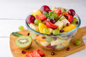 Healthy fresh fruit salad in glass bowl on white wooden background.