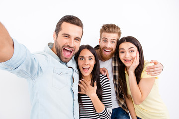 Group of excited friends making selfie on the camera of smartphone showing great emotions of amazement and excitement on white background in casual clothes