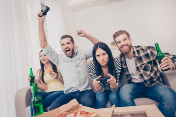 Young people having home party with video games, pizza and beer. They show different emotions because of who lost and who won