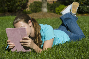 Naklejka na ściany i meble Teenage girl relaxes on the grass with a tablet