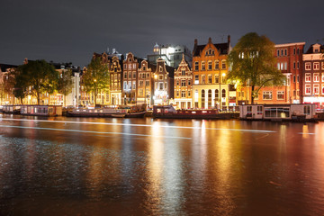 Fototapeta na wymiar Amsterdam canal Amstel with typical dutch houses, houseboat and luminous track from the boat at night, Holland, Netherlands.