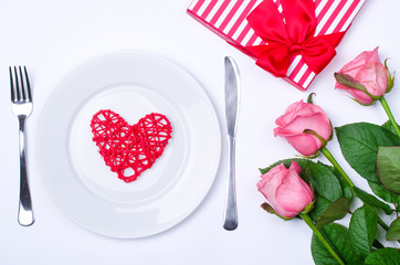 Romantic dinner: plate, cutlery and roses on a white background.