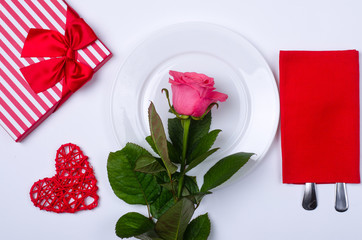 Romantic dinner: plate, cutlery and rose on a white background.