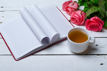 Spring festive background: a cup of tea, pink roses and a notebook.