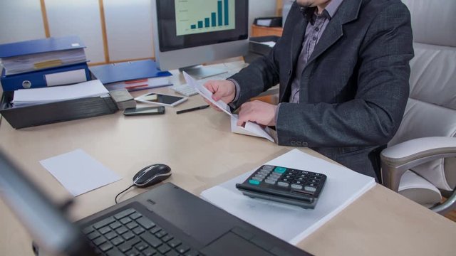 A businessman is putting some documentation in an envelope and then he is closing it. He is smiling.
