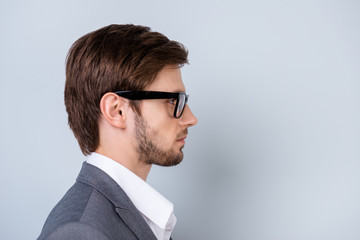 Side-view close-up portrait of  young successful serious man in glasses standing on gray background