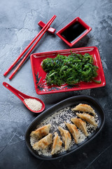 Fried gyoza dumplings with seaweed salad, sesame seeds and dipping sauce, vertical shot, selective focus