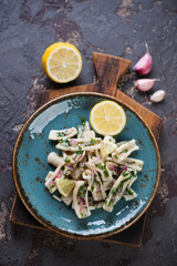 Salad with boiled calamari and onion filling served on a turquoise plate, top view on a brown stone background
