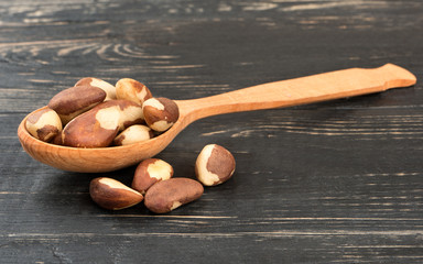Spoon filled with Brazilian nuts on a wooden background