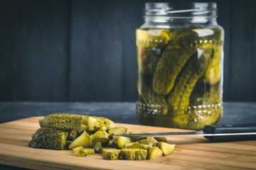 Cucumbers or pickled gherkins with a knife on a wooden cutting board. Blue gray background. Bank with cucumbers.