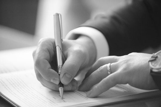 foto b/n di una mano che firma con una penna un documento