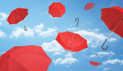 Many open red umbrellas falling from the blue sky dotted with clouds.