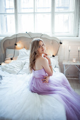Naklejka premium Very beautiful bride in a delicate purple dress sitting on the bed. Luxury bedroom decor with candles.