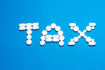 Word TAX made of white pills on blue background