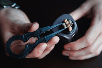 male master installs a coil. Spiral for electronic evaporator and cigarette. Vape, vaping. Firing a...