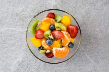Fruit salad in crystal bowl on gray stone. Top view
