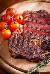 Sliced medium rare grilled Beef steak Ribeye with cherry tomatoes on cutting board, selective focus