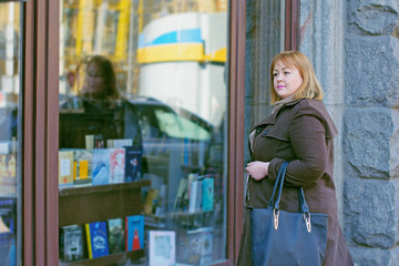 Obraz na płótnie Canvas Cute woman with red hair of size plus size walks through the mazaginas looks in showcases chooses things like shopping and beautiful stylish accessories reflects on her appearance 