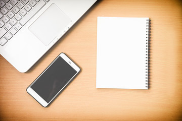 Busiiness notebook computer and notebook paper message with smart phone on wooden desk background with film effect