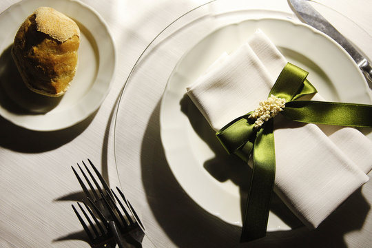 Apparecchiatura  sobria con piatti bianchi e fiocco verde intorno al  fazzoletto, piatto bianco con il pane