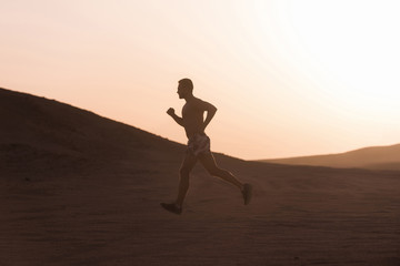 Fototapeta na wymiar Man runner running in dune at sunset