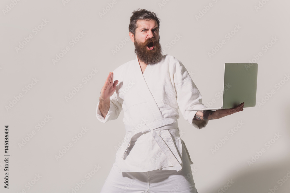 Wall mural bearded angry karate man in kimono with laptop