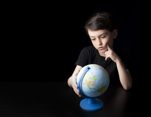 Low key portrait of young boy isolated on black background. Plenty of space left for copy. Thinking about the future of the world, contemplating the globe