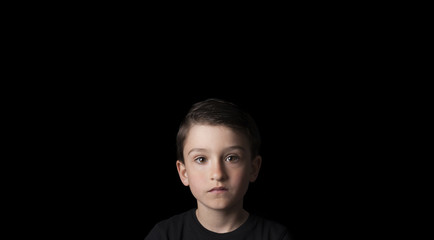 Low key portrait of young boy isolated on black background. Plenty of space left for copy. for Flyers, posters and other commercial purposes