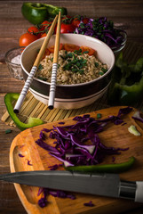 Brown rice with vegetables and chopsticks on a wooden background
