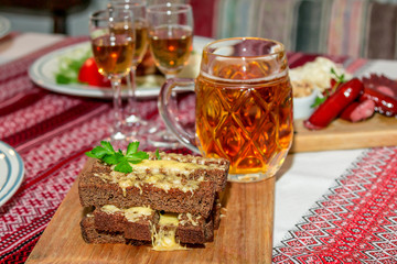 Hot snack for beer.  Roasted brown whole wheat bread with melted cheese and parsley on a wooden board and mug of beer.