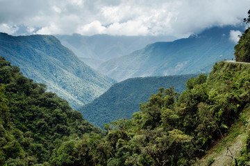Panoramic view of the mountainous landscape of North Yongas and a cyclist on the Death Road on the far right, Bolivia