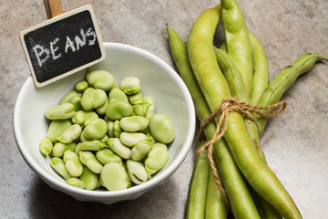 Habas crudas en cuenco blanco y vainas. Vista superior