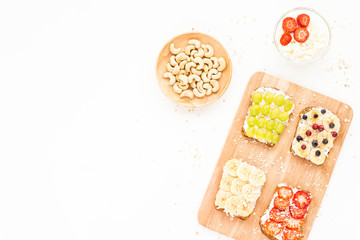 Healthy fruit breakfast. Yogurt fruit toasts with banana, cream cheese, grapes, berry, strawberry, cereals and nuts on white background. Top view, flat lay.