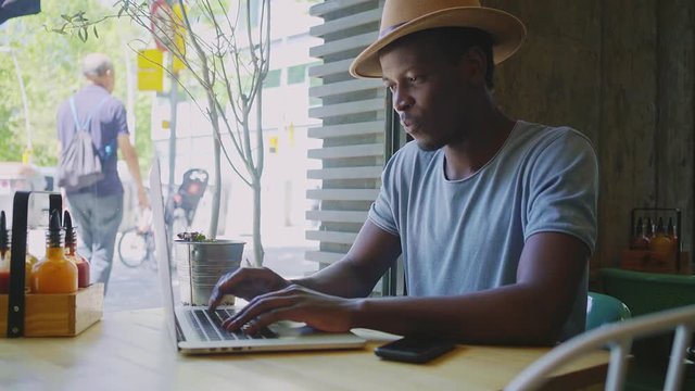 Young black man sits in a trendy cafe on his day off work he is motivated and works extra hours, he waits for an important message on social media in his electronic devices