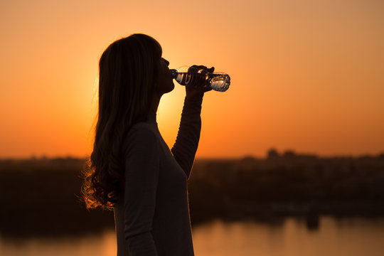 Silhouette of a woman drinking water at the sunset.