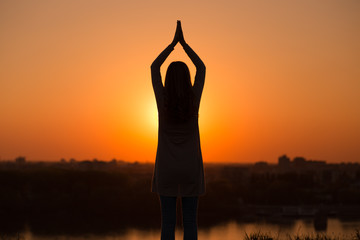 Silhouette of a woman meditating at the sunset.