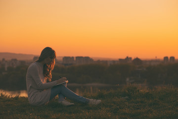 Woman enjoys writing at her  notebook with a sunset over the city.