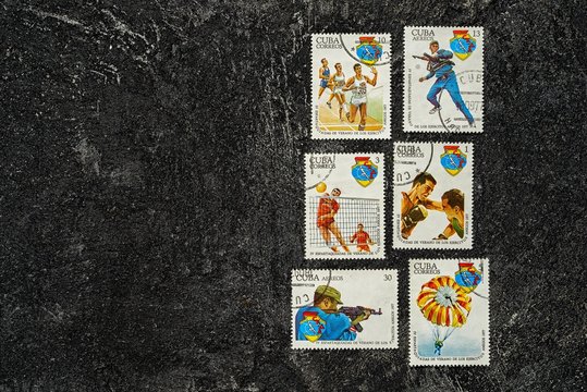 Set of randomly lying postage stamps printed in Cuba shows sportsmen, devoted to 4 Spartakiad,  series, circa 1977, on a dark black cement background.