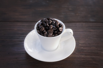 Coffee beans in cup on wooden background